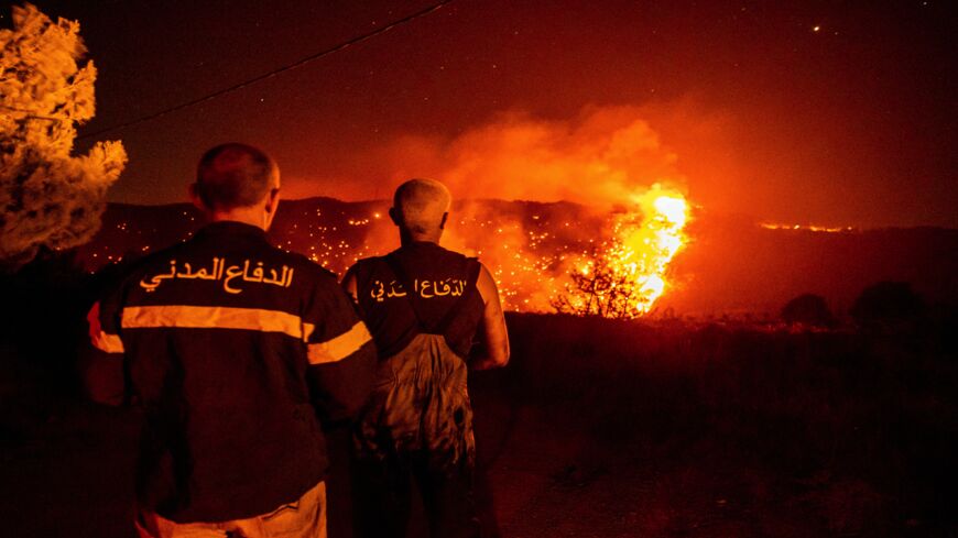 Civil Defense personnel monitor a wildfire burning through hills on July 28, 2021, in Qobayat, Lebanon. 