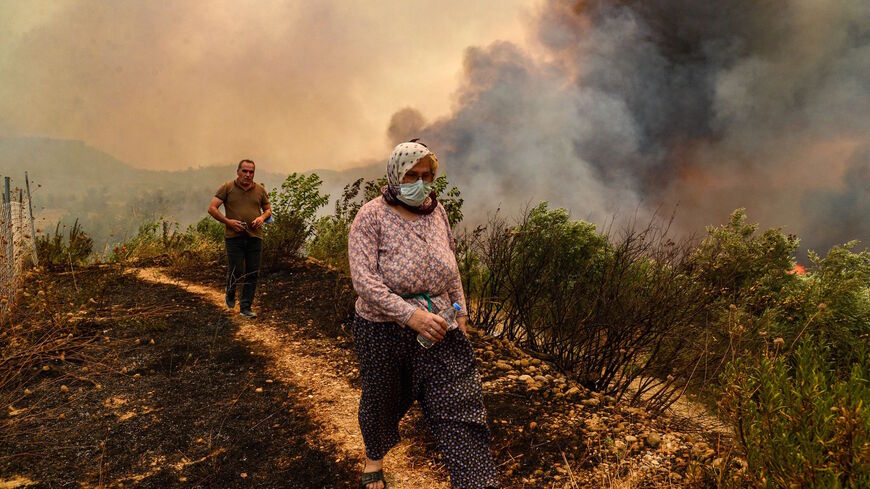 People walk past flames in a burning area during a massive forest fire which engulfed a Mediterranean resort region on Turkey's southern coast near the town of Manavgat, on July 29, 2021.