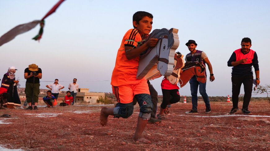 Displaced Syrian children run with a cutout of horseheads during the so-called "Camp Olympics 2020."