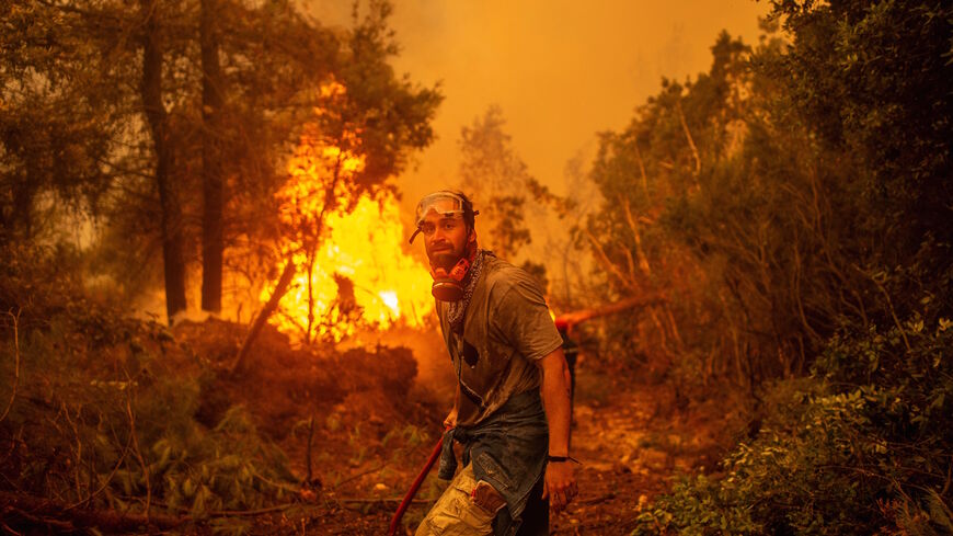A volunteers holds a water hose near a burning blaze as he tries to extinguish a fire in the village of Glatsona on Evia (Euboea) island, on Aug. 9, 2021. 