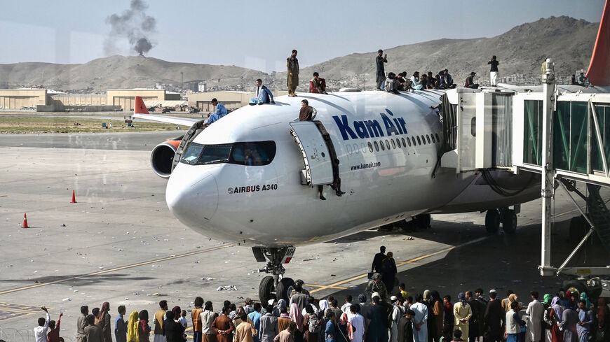 Afghan people climb atop a plane as they wait at the Kabul airport in Kabul on August 16, 2021, after a stunningly swift end to Afghanistan's 20-year war, as thousands of people mobbed the city's airport trying to flee the group's feared hardline brand of Islamist rule. 