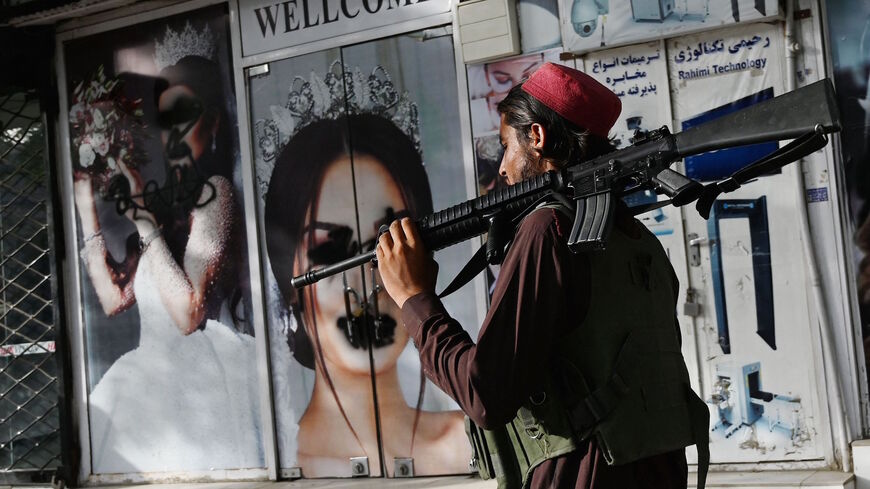 A Taliban fighter walks past a beauty saloon with images of women defaced using a spray paint in Shar-e-Naw in Kabul on Aug. 18, 2021.