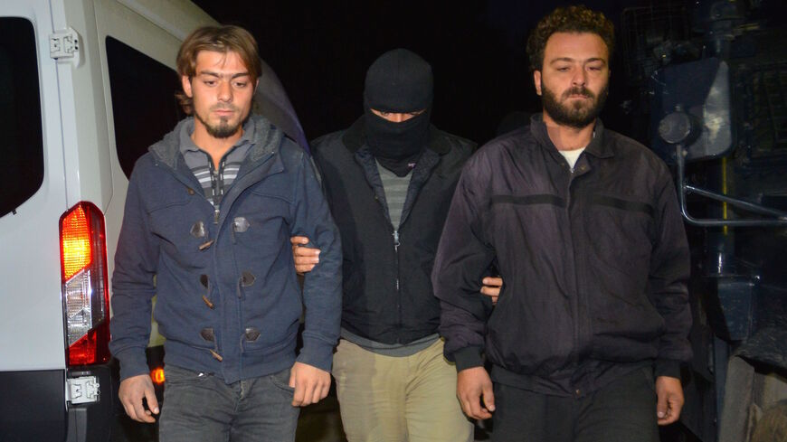 A masked Turkish special force police officer detains two men during a house raid to arrest suspected members of the Islamic State group, in Adana, on Nov. 10, 2017.