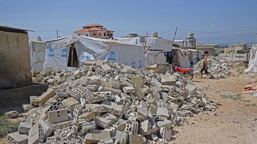 A Syrian refugee walks past the rubble of demolished concrete walls at a make-shift camp in the town of Rihaniyye in Lebanon's Akkar governorate on Aug. 9, 2019. 