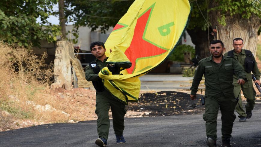 Syrian Kurdish fighters walk carrying a People's Protection Units (YPG) yellow flag in the Syrian Kurdish town of Kobane.