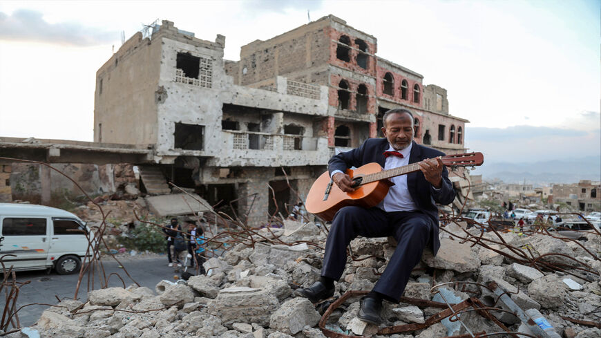 A Yemeni artist sitting atop the rubble of a collapsed buiding plays the guitar during a street performance, Taez, Yemen, Dec. 6, 2019.