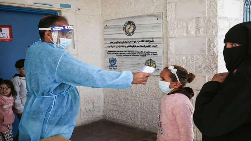 An employee of the United Nations Relief and Works Agency for Palestine Refugees measures the body temperature of a girl as people arrive to receive the Sputnik V COVID-19 vaccine at UNRWA's clinic in Rafah camp, southern Gaza Strip, March 3, 2021.