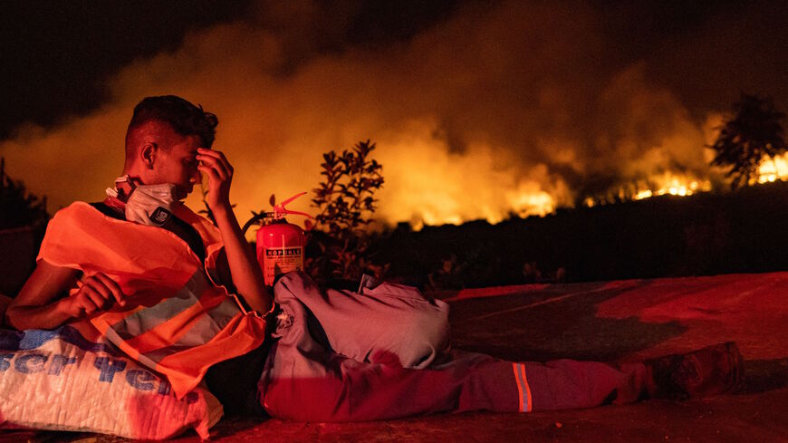 A volunteer rests as flames rise from a forest burning in the background near Akcayaka, a town in the Mugla province, on Aug. 6, 2021.