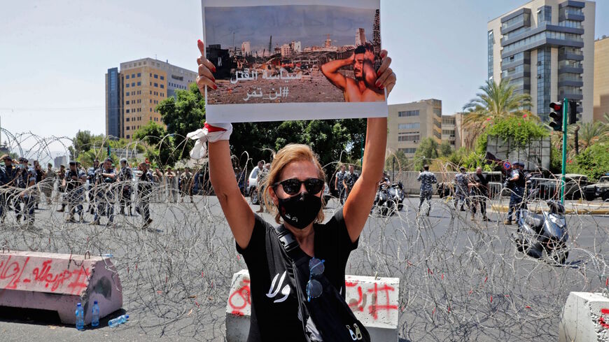 A woman holds a sign showing a photo of a man reacting at the scene of the 2020 Beirut port blast, as protesters and family members of the 2020 Beirut port blast gather for a demonstration near the UNESCO palace in the Lebanese capital on Aug. 12, 2021, ahead of a parliamentary meeting on the blast investigation. 