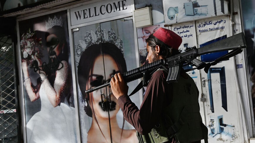 A Taliban fighter walks past a beauty salon with images of women defaced using spray paint in Shar-e-Naw in Kabul on Aug. 18, 2021. 