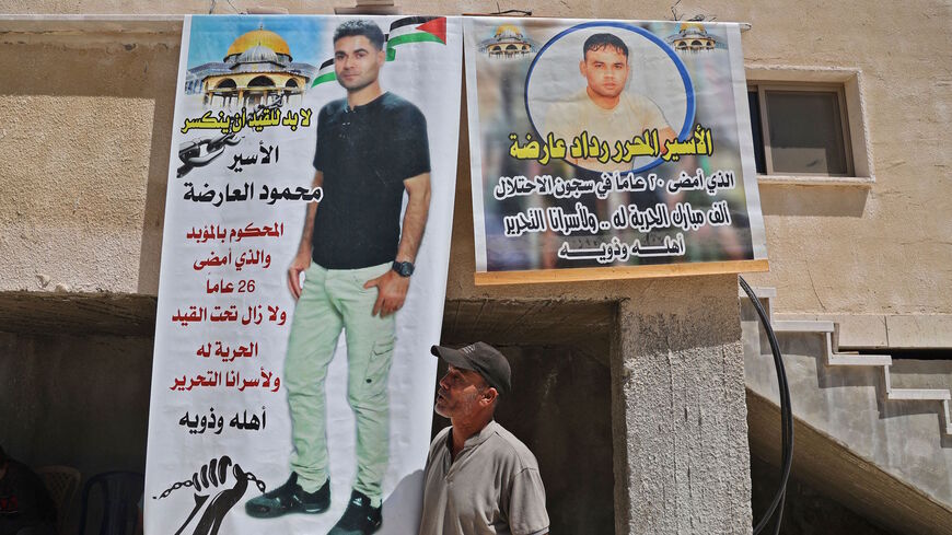 A relative of Mahmud al-Ardeh, one of six Palestinian prisoners who escaped from Israel's Gilboa prison, stands next to a banner showing him (L) and another prisoner, Raddad al-Ardeh, by his home in the village of Arabah, south of Jenin in the occupied West Bank on Sept. 8, 2021.