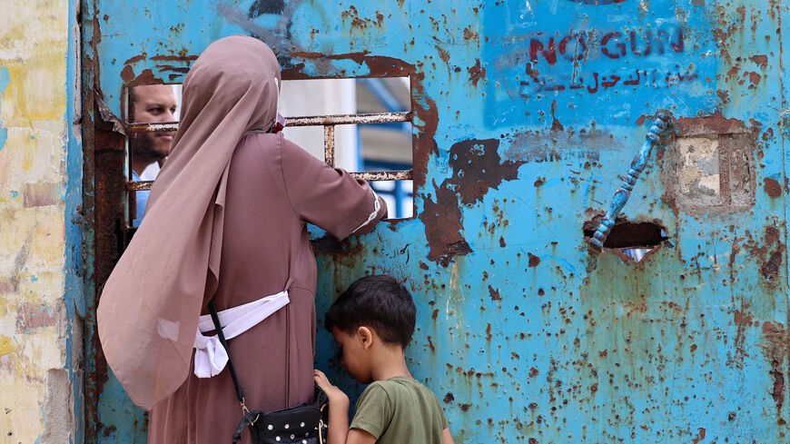 A Palestinian woman and her child stand next to a window of an aid distribution centre run by the United Nations Relief and Works Agency (UNRWA) in Gaza City, on Sept. 16, 2021.