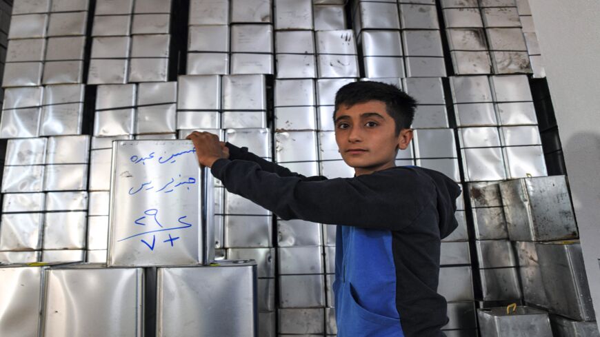 A boy looks on next to a stack of olive oil containers at an oil pressing facility belonging to Syrian Kurds.