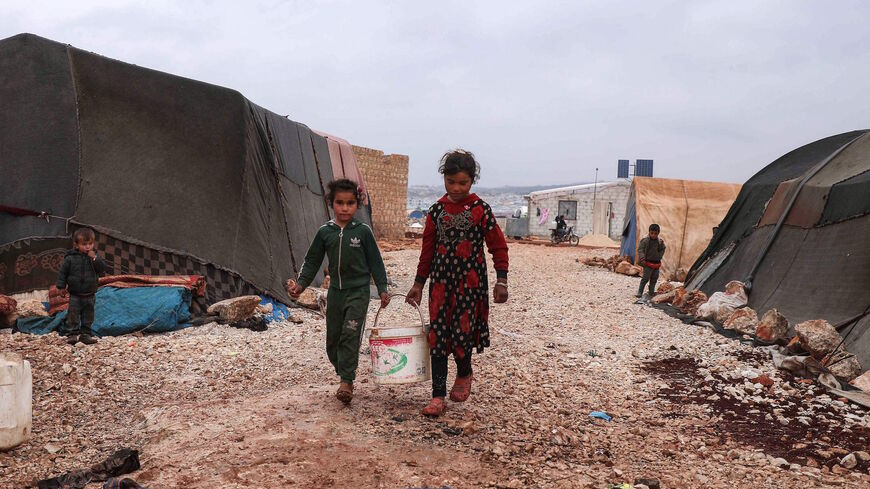 Children on Nov. 20, 2021, carry a bucket of water, in the Bardaqli camp for displaced people in the town of Dana in Syria's northwestern Idlib province, as winter approaches.