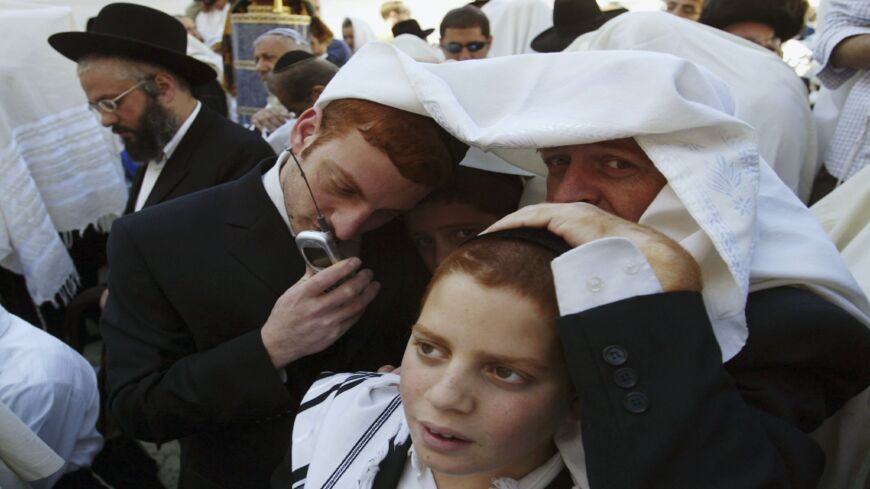 An Israeli ultra-Orthodox Jew talks on a mobile phone as others pray during the Passover blessings.