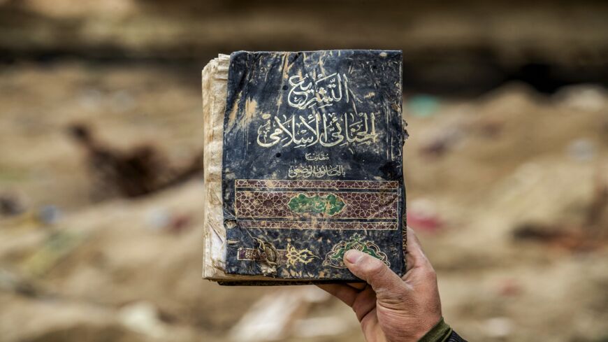 A fighter from the SDF carries a book on Islamic criminal legislation said to have belonged to the Islamic State, recovered in Baghuz, Syria, on March 13, 2020.