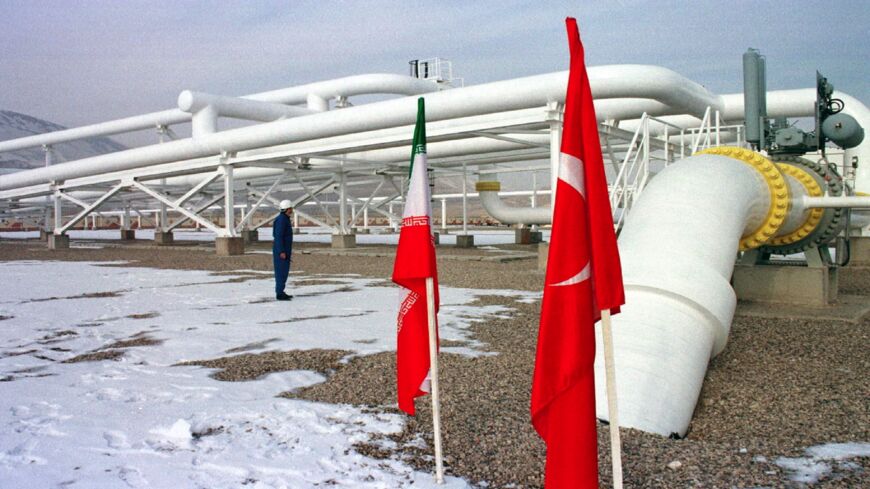 An Iranian worker stands in front of gas pipelines next to the flags of Turkey (R) and Iran.