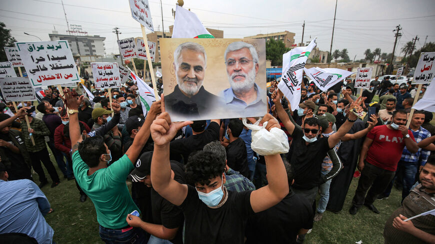 A supporter of the Iran-backed Hashed al-Shaabi (Popular Mobilisation) paramilitary forces stands holding a picture showing the faces of (L to R) slain Iranian commander Qasem Soleimani and Iraqi paramilitary commander Abu Mahdi Al-Muhandis during a demonstration outside the entrance to the Iraqi capital Baghdad's highly-fortified Green Zone on Nov. 7, 2020, demanding the departure of remaining US forces from Iraq. 