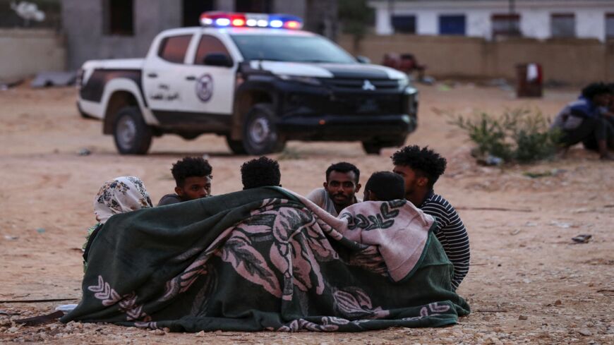 African migrants huddle under a blanket at a makeshift shelter in the capital Tripoli's suburb of Ain Zara, on Oct. 9, 2021. 