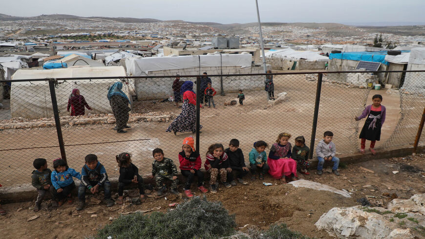 Children sit along a fence at a camp for displaced Syrians in Deir Hassan village, in Idlib's northern countryside near the Turkish border, March 5, 2020.