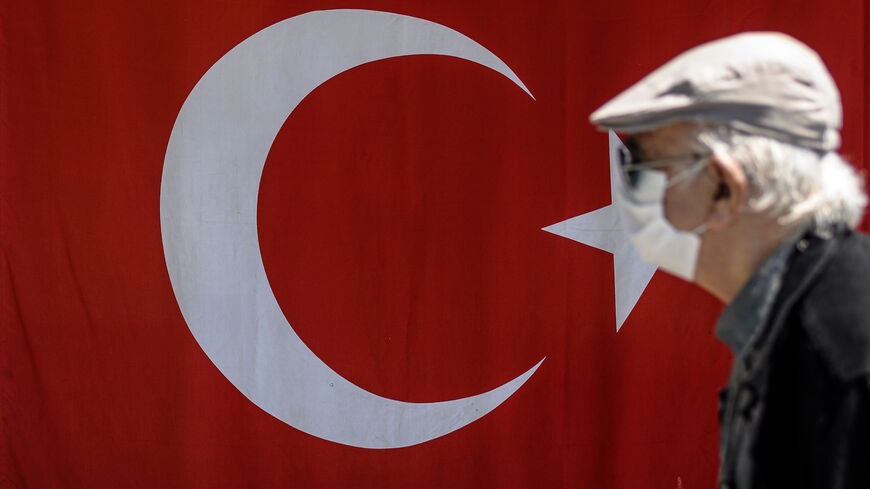 An elderly man wearing a protective face mask, walks past the Turkish flag on May 10, 2020, at Besiktas in Istanbul.