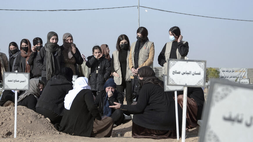 Women mourn by a grave during a mass funeral for Yazidi victims of the Islamic State (IS) group whose remains were found in a mass grave, in the northern Iraqi village of Kojo in Sinjar district, on Dec. 9, 2021. 