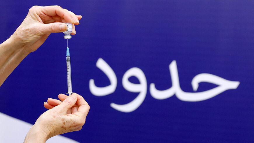 An Israeli nurse prepares a dose of the Pfizer-BioNTech COVID-19 coronavirus vaccine, with Arabic writing in the background showing the last word of the slogan, "Hope without limit," at the Sheba Medical Center, Ramat Gan, near Tel Aviv, Israel, Dec. 27, 2021.