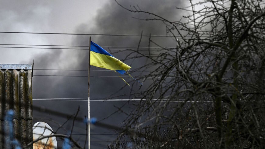 An Ukrainian flag waves in front of smoke rising from a bombed warehouse in the town of Stoyanka, west of Kyiv, on March 4, 2022.