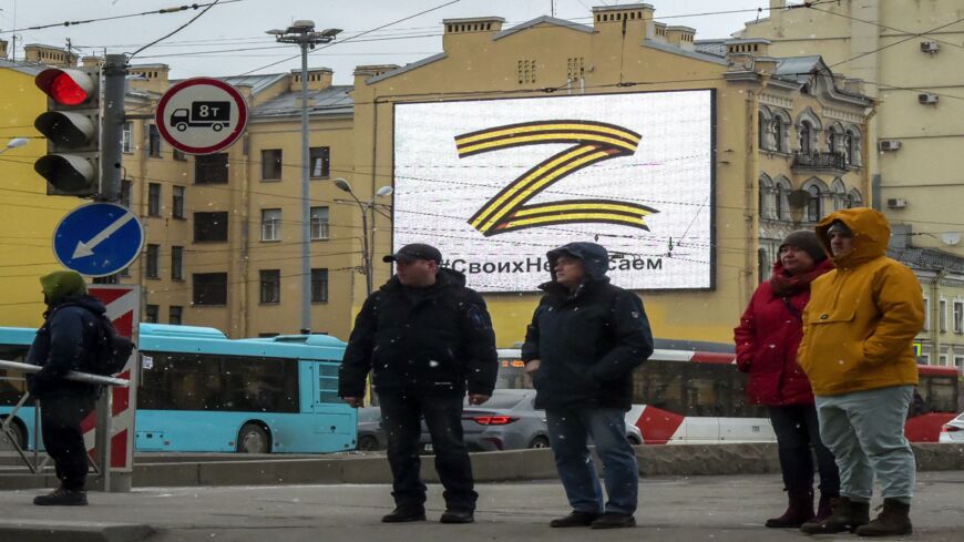 Pedestrians cross a street in front of a billboard displaying the symbol "Z."