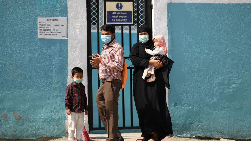 Parents wearing protective masks and their children arrive at a school entrance.