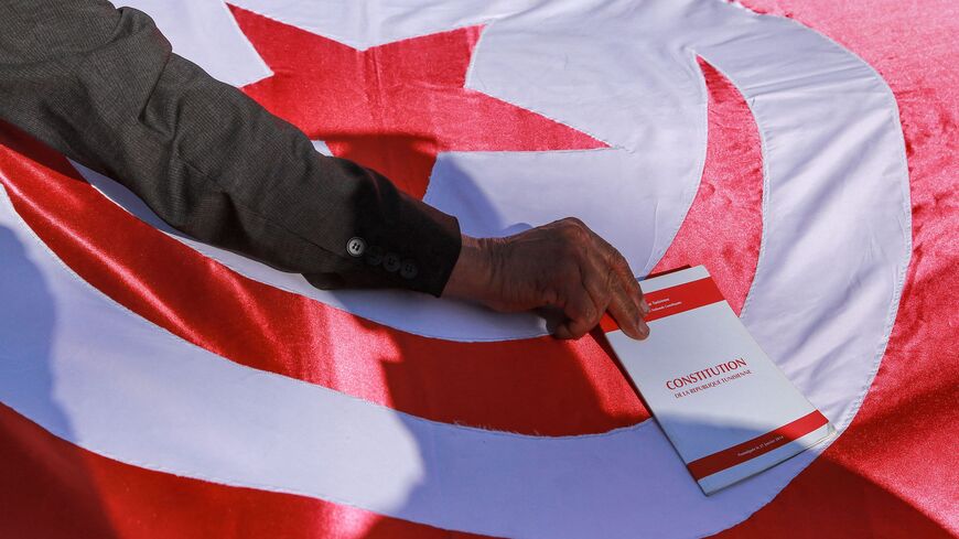 A man places a copy of the Tunisian Constitution atop a Tunisian national flag.