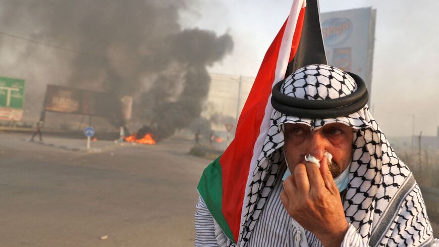 A protester holds a tissue to his nose while holding a Palestinian flag near a tire fire.