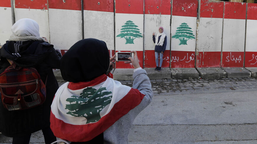 A woman takes a photograph of another standing in front of a wall of cement blocks, set up by Lebanese security forces to bar a street leading to the parliament building, Beirut, Lebanon, Jan. 24, 2020.
