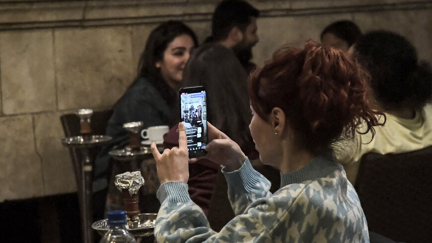 A woman uses her phone to livestream a traditional "hakawati" storyteller performing late after midnight during the Muslim holy fasting month of Ramadan, at the historic Dar Halabia Hotel in the Bab Antakya area of the Old City of Aleppo, Syria, April 12, 2022.