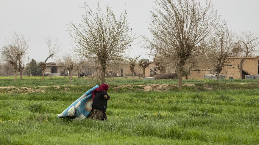 A woman carries a quilt as she crosses a field in the eastern Syrian village of Baghouz on March 13, 2020, a year after the fall of the Islamic State's (IS) caliphate. 