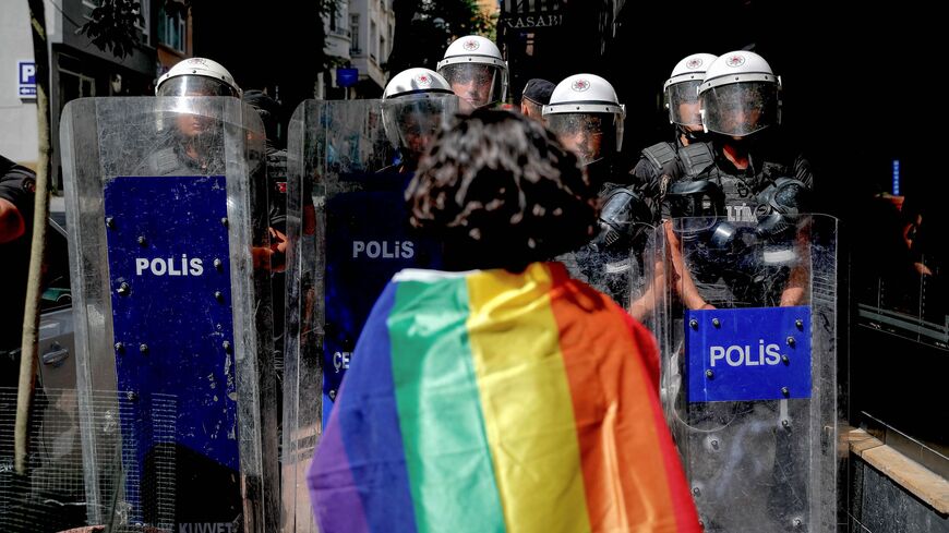 A participant faces riot policemen wearing a rainbow flag during a Pride march in Istanbul, on June 26, 2022. 
