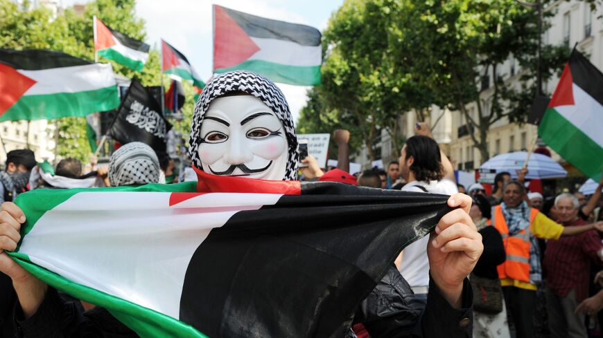 A protester wearing a mask of the Anonymous computer hacking activists group and holding the Palestinian flag.
