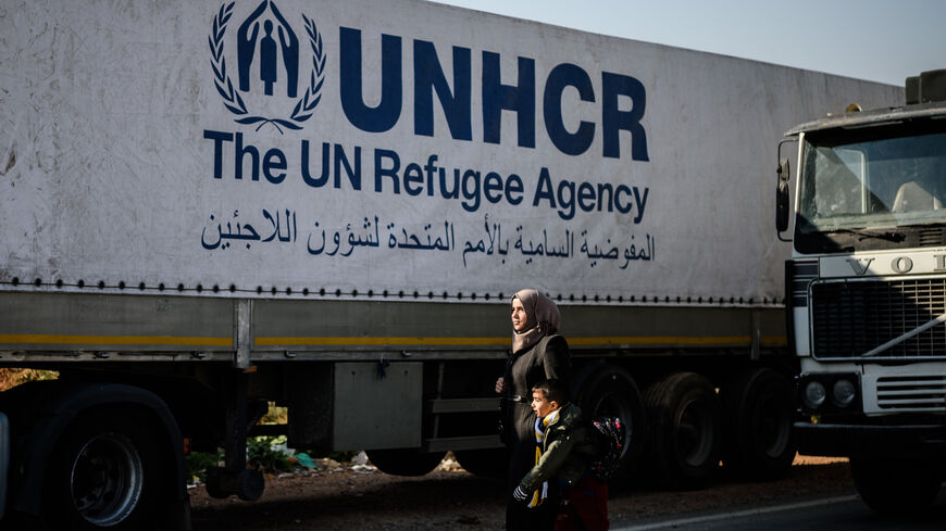 A Syrian woman with her child walks near a Syrian-bound truck loaded with humanitarian aid.