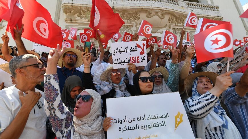Tunisian protesters raise flags and placards on July 23, 2022, during a demonstration along Habib Bourguiba avenue in the capital Tunis, against their president and the upcoming July 25 constitutional referendum