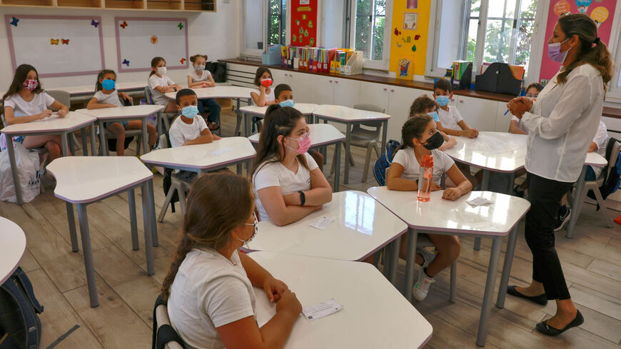 An Israeli teacher welcomes pupils wearing protective face masks upon their return to the new school year amid a surge of coronavirus cases in Israel, at Beit Hakerem Israeli elementary school in Jerusalem, Sept. 1, 2021.