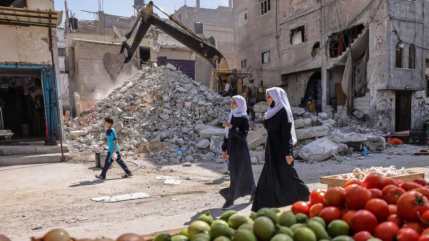 Women walk past a vegetable stand, as workers clear the rubble of a building destroyed by Israeli bombing in May 2021, Rafah, southern Gaza Strip, Sept. 30, 2021.