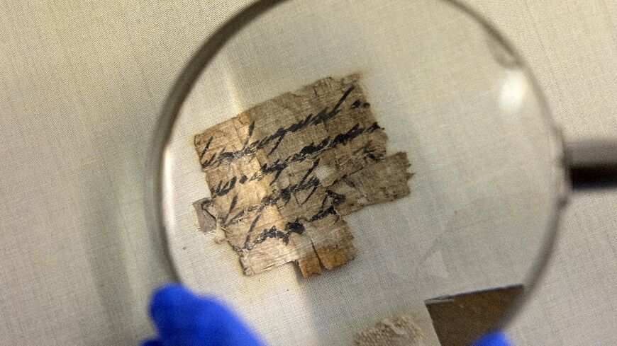 An Israel Antiquities Authority conservator views under a magnifying glass the papyrus fragment at its conservation lab in Jerusalem