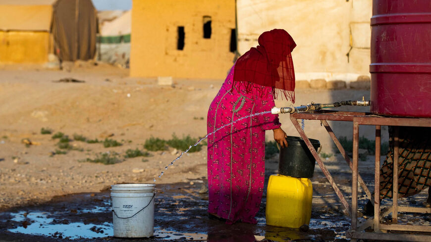 A Syrian woman fills a container with water at the Sahlah al-Banat camp in the countryside of Raqqa, northern Syria, Sept. 19, 2022.