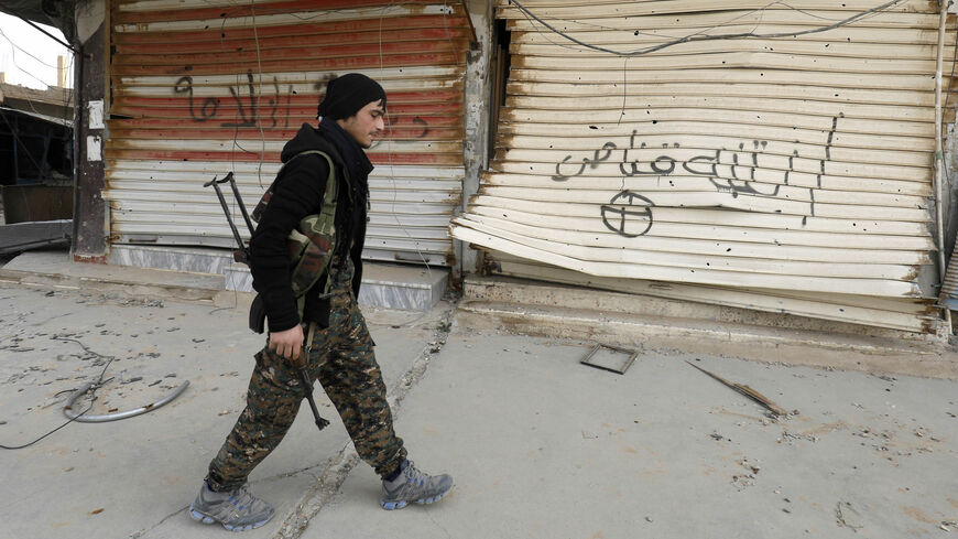 A fighter from the Syrian Democratic Forces (SDF) walks past shops with their fronts painted with the Arabic phrases "beware a sniper" and "caliphate state," after the Kurdish-led and US-backed SDF retook the city from Islamic State fighters, Hajin, Deir ez-Zor province, Syria, Jan. 27, 2019.