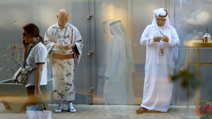 A Japanese and an Emirati man in traditional clothes check their phones at the Arabian Travel Market.