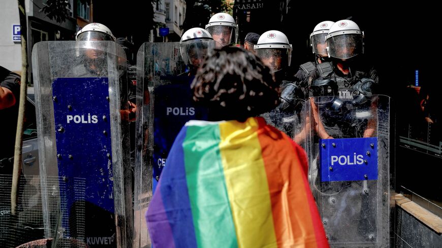 A participant faces riot policemen wearing a rainbow flag during a pride march in Istanbul, on June 26, 2022. 
