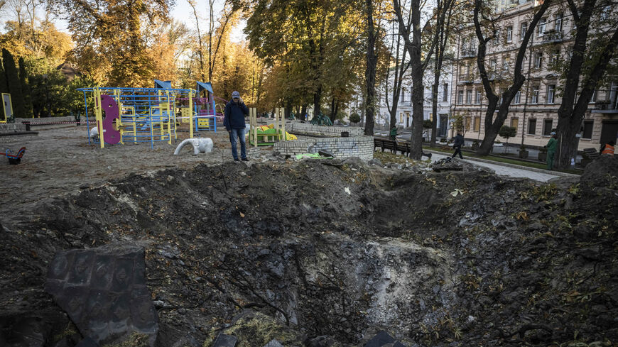 People look at the crater left by a missile strike on a playground in Taras Shevchenko Park the day before, Kyiv, Ukraine, Oct. 11, 2022.