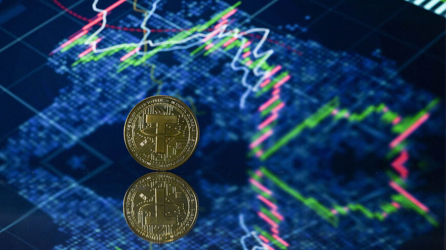 An illustration picture taken in London shows a gold plated souvenir cryptocurrency Tether (USDT) coin arranged beside a screen displaying a trading chart, May 8, 2022.