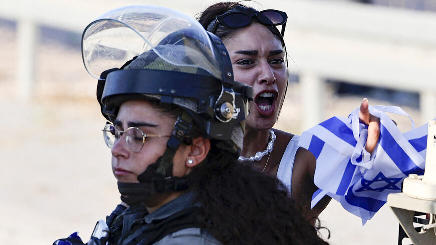 An Israeli settler surrounded by Israeli security forces holds national flags.