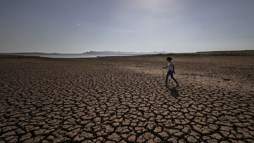 A woman walks over cracked earth at al-Massira dam in Ouled Essi Masseoud village, some 140 kilometres (85 miles) south from Morocco's economic capital Casablanca, on August 8, 2022 amidst the country's worst drought in at least four decades. - Residents of Morocco's Ouled Essi Masseoud village are suffering from a series of successive droughts, prompting them to rely solely on sporadic supplies in public fountains and from private wells. The situation is critical, given the village's position in the agricu